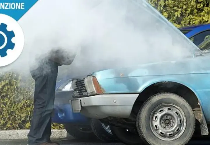 Uomo guarda motore fumante di un'auto blu, probabile perdita liquido refrigerante.