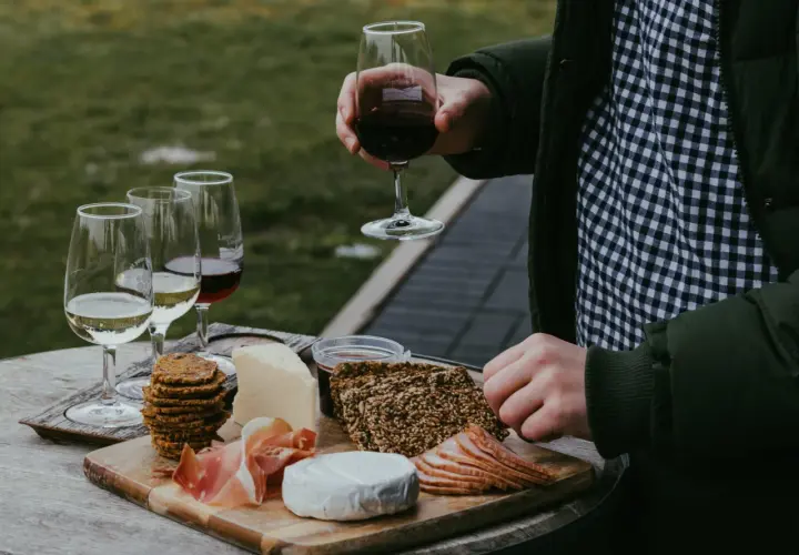 Un plateau de fromages, charcuteries et biscuits accompagne un verre de vin rouge. Une dégustation parfaite de vin et volailles en plein air.