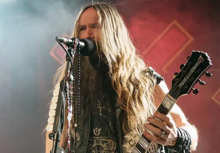 Zakk Wylde, wokalista i gitarzysta, z długimi blond włosami i naszyjnikami, gra na gitarze podczas koncertu.