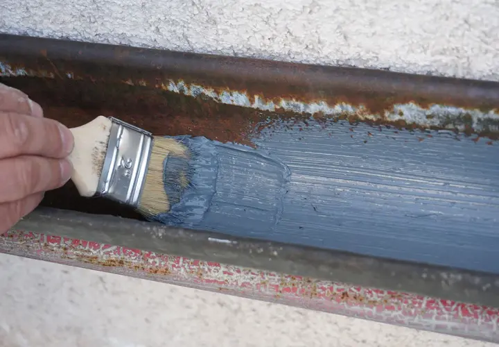 Hand streicht mit Pinsel graue Farbe auf rostige Dachrinne zum dachrinne abdichten.