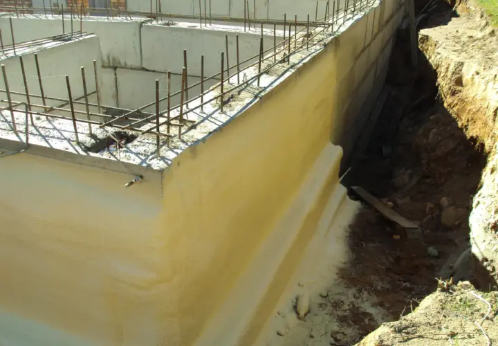 Zastosowano izolację pionową fundamentów. Widać zbrojenie i betonowe ściany fundamentowe, a obok wykop z ziemią.
