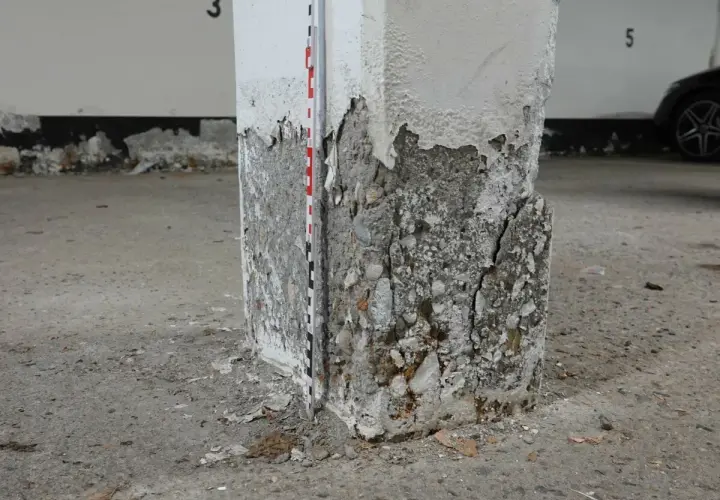 Betonsäule mit starker Abplatzung und Rissen, Messlatte zur Schadensdokumentation. Die STB Decke ist hier stark beschädigt.