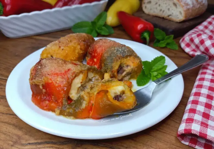 Involtini di peperoni ripieni, dorati e succulenti, serviti su un piatto bianco con menta fresca.