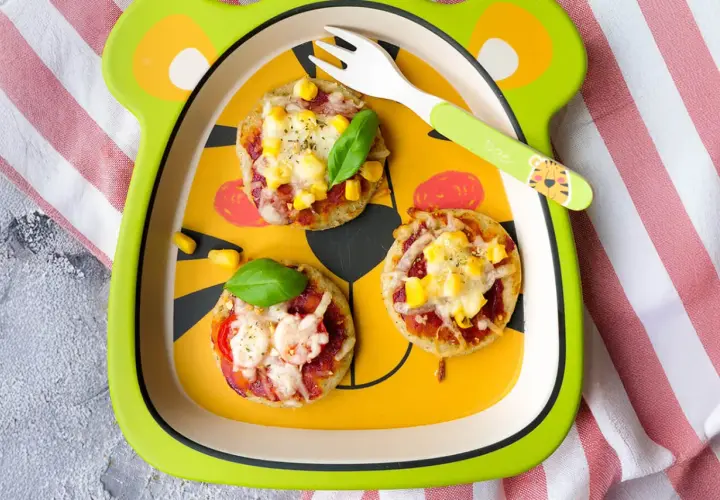 Schneller Pizzatag mit Quark: Kleine Mini-Pizzen mit Mais und Käse auf einem lustigen Teller, bereit zum Genießen.