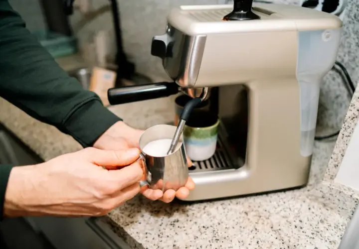 Ręce spieniają napój owsiany barista w metalowym dzbanku, przygotowując kawę.