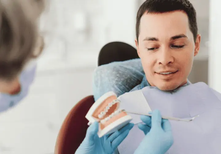 Dentysta pokazuje pacjentowi model szczęki z aparatem, omawiając, czy trzeba usuwać ósemki do aparatu ortodontycznego.