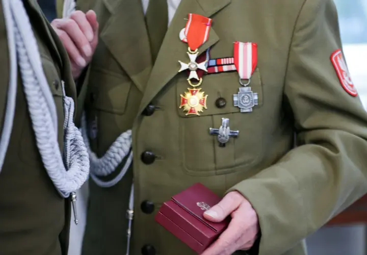 Żołnierz w mundurze z licznymi odznaczeniami wojskowymi na piersi. W dłoni trzyma małe, czerwone pudełko.