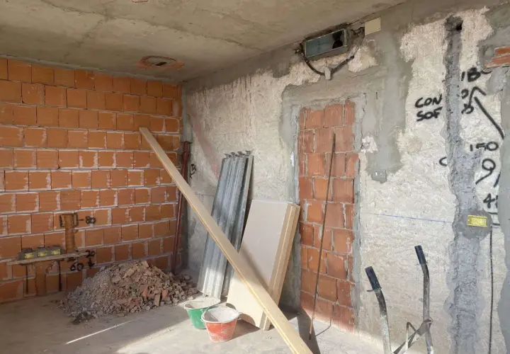 Interno di una casa in fase di ristrutturazione: pareti in mattoni a vista, cumulo di macerie, secchi, assi di legno e materiale edile.