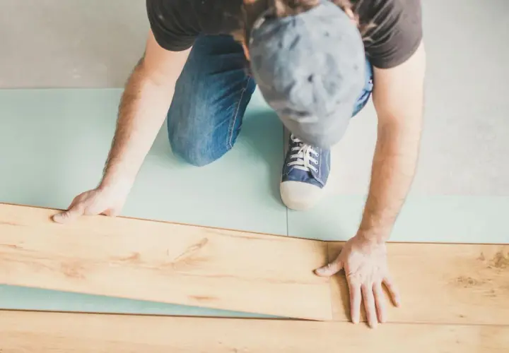 Uomo posa pannelli per come isolare il pavimento dal freddo. Sottile strato isolante azzurro sotto le assi di legno.