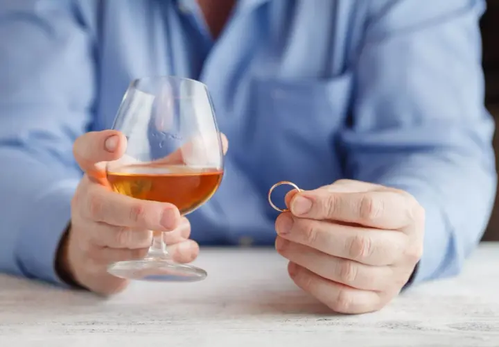 Mężczyzna trzyma kieliszek z alkoholem i obrączkę. Rozważania o rozdzielności majątkowej a alimentach na dziecko z poprzedniego związku.