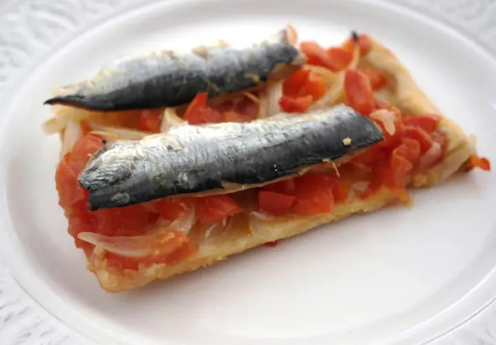Rebanada de masa con tomate, cebolla y dos sardinas enteras, un plato que recuerda a las sardinas San Juan.