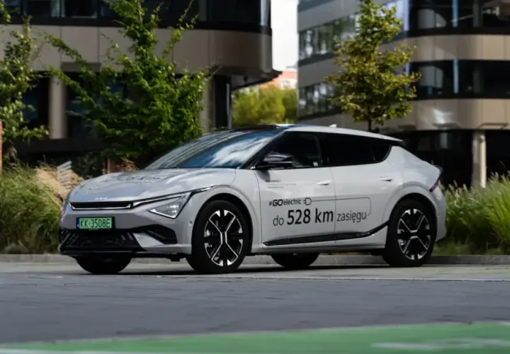 Biały Kia EV6 zaparkowany przed nowoczesnym budynkiem, z napisem "#GOelectric do 528 km zasięgu".