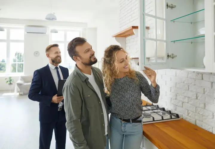 Couple inspecte une cuisine lors d'un état des lieux avant signature notaire. Un agent immobilier les accompagne.