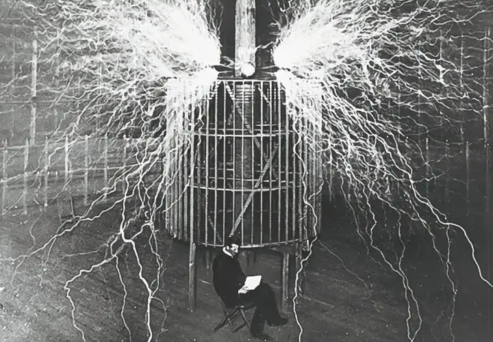 Nikola Tesla w klatce, otoczony wyładowaniami elektrycznymi, badał, kto wynalazł prąd.
