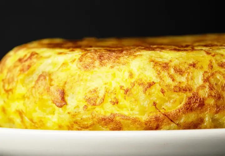 Złocista tortilla de patatas, pachnąca ziemniakami i jajkami, kusi apetycznym wyglądem na białym talerzu.