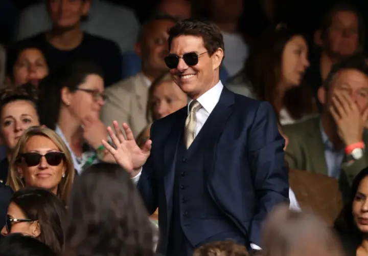 Tom Cruise w garniturze, w okularach przeciwsłonecznych, macha do publiczności. Zastanawiasz się, ile zarabia Tom Cruise?