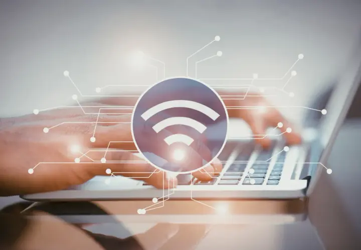 Dłonie piszące na laptopie, symbol Wi-Fi i schemat połączeń. Dowiedz się, jak sprawdzić pasmo Wi-Fi w telefonie.