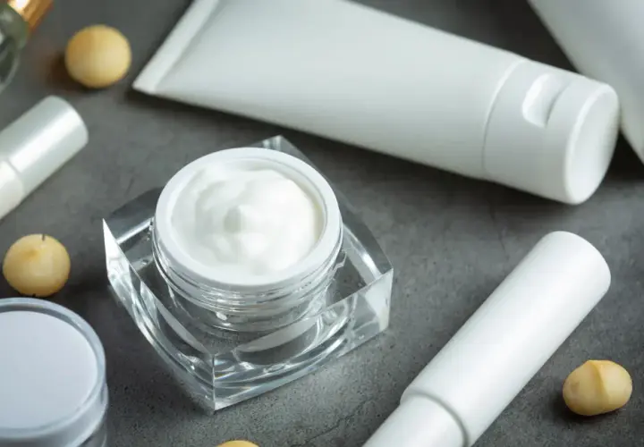 Crema blanca en un frasco de cristal, tubos y bolitas doradas. Descubre qué es el pantenol y sus beneficios para tu piel.
