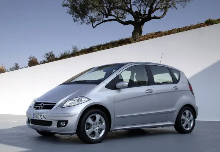 Srebrny Mercedes W169 stoi na tle białej ściany i drzewa oliwnego.