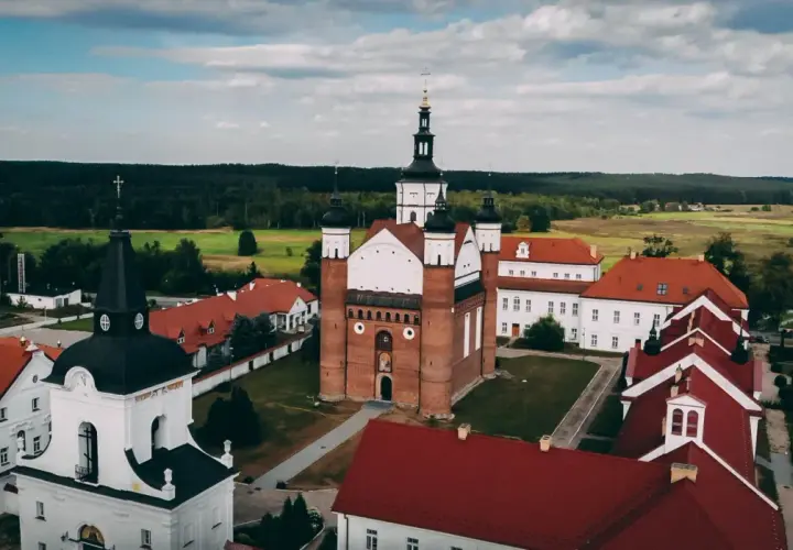 Architektura sakralna w okolicach Białegostoku: klasztor z ceglaną bazyliką i białymi wieżami, otoczony zielenią i polami.