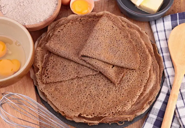 Pile de crêpes de sarrasin, avec des ingrédients pour la pâte à crêpe sarrasin : farine, œufs, beurre.