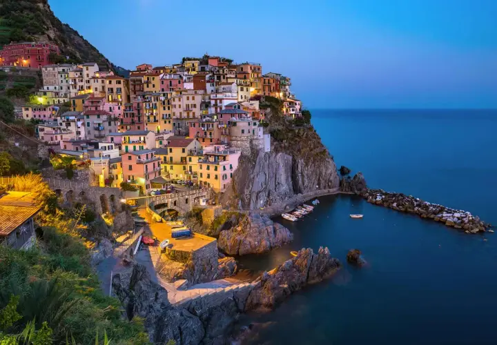 Village coloré accroché à la falaise, au crépuscule, dans le site de Cinque Terre. Bateaux dans le port, mer bleue.