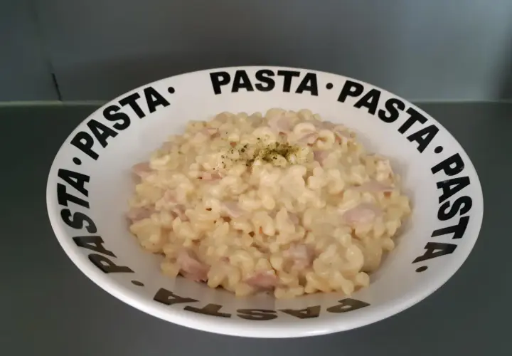 Un crémeux risotto coquillette jambon, garni d'herbes, servi dans une assiette au message "PASTA" répété.