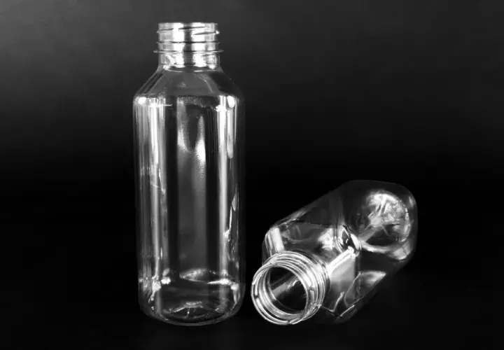 Dwie puste, przezroczyste butelki PET o pojemności 300 ml na czarnym tle. Jedna stoi pionowo, druga leży.