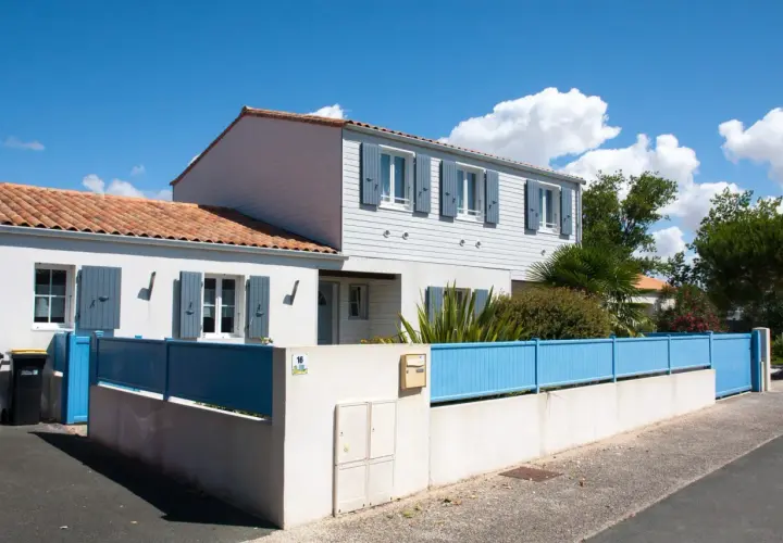 Maison année 70 rénovée, avec volets bleus et clôture assortie. Avant, elle était plus sombre.