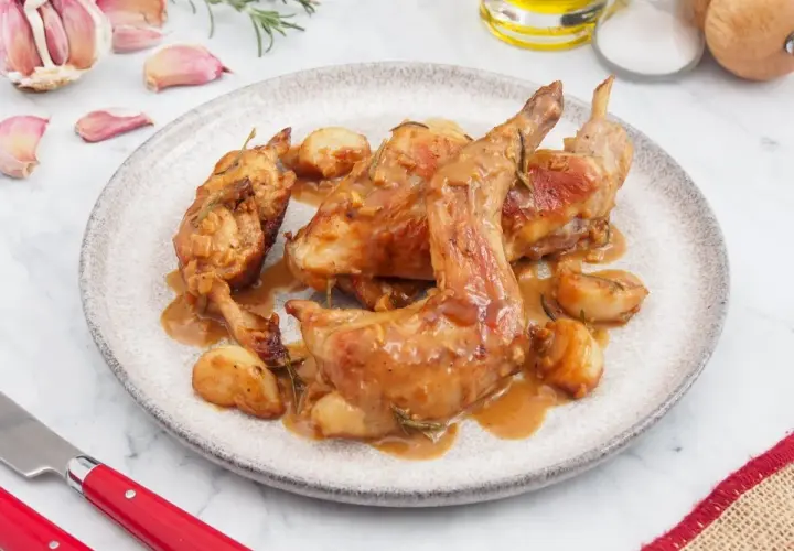 Delicioso conejo al ajillo servido en un plato, con ajos enteros y romero. Una receta tradicional lista para disfrutar.