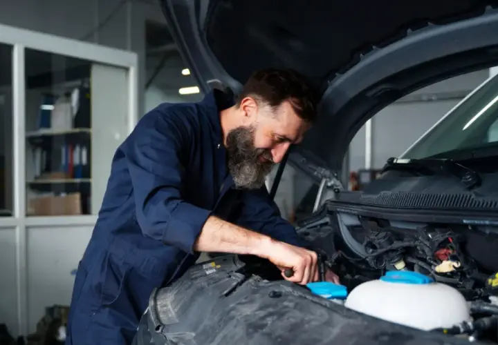 Mechanik z brodą pracuje przy silniku. Zastanawiasz się, ile kosztuje wymiana chłodnicy w samochodzie?