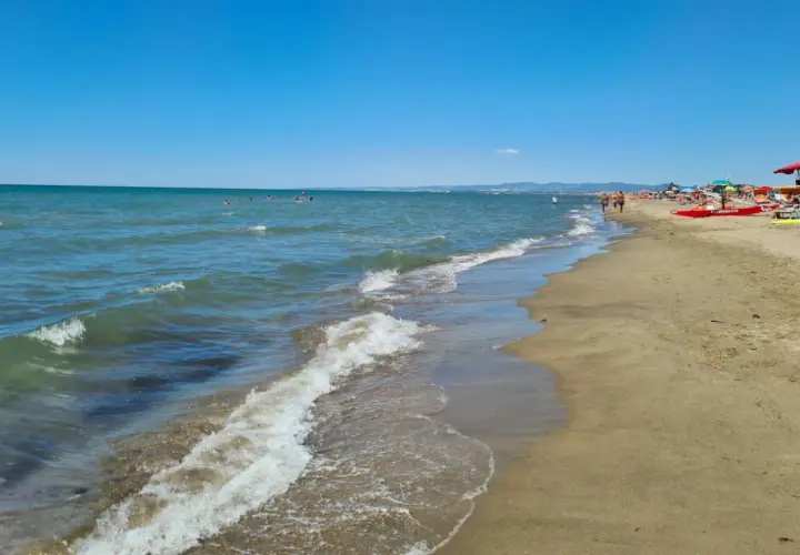 Plage de Fregene, mer bleue, sable doré, parasols et baigneurs profitant du soleil.