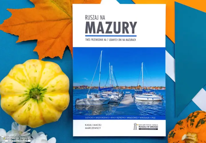 Okładka przewodnika po Mazurach z widokiem na żaglówki i jesienne dekoracje.