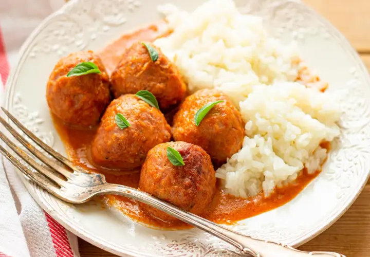 Albondigas a la jardinera con arroz blanco, decoradas con hojas verdes. Un plato casero y apetitoso.