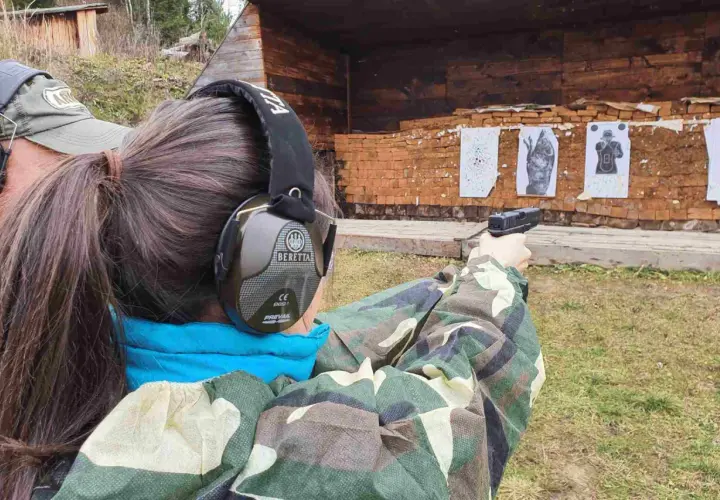Strzelanie z broni na strzelnicy. Kobieta w słuchawkach ochronnych celuje z pistoletu do tarcz.