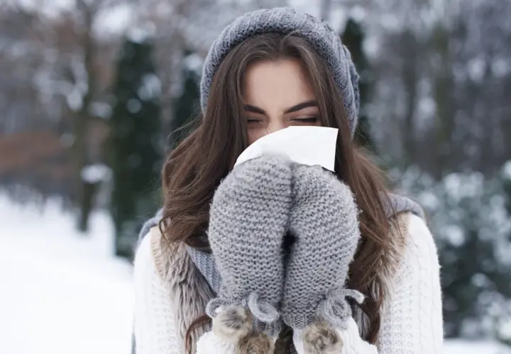 Femme en bonnet et moufles d'hiver se mouchant, un rappel pour prévenir le rhume.