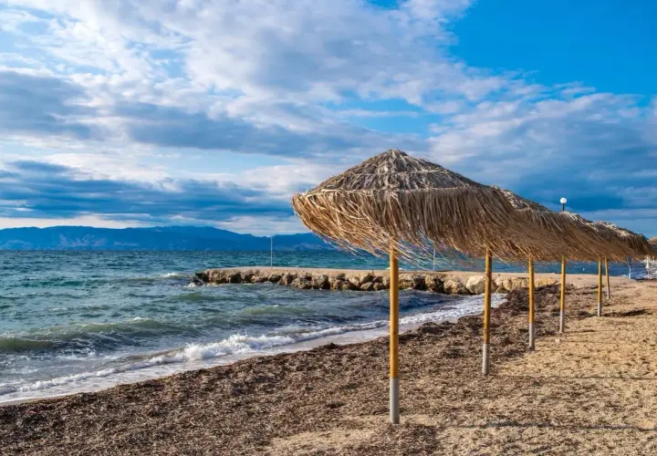 Słomiane parasole na plaży Angela Beach Korfu, morze i góry w tle.