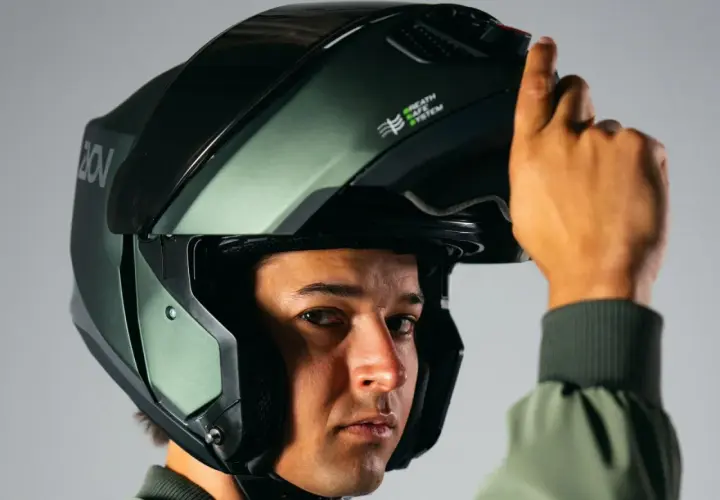 Un hombre se ajusta un casco de moto verde oscuro, similar a un casco guardia civil, con el sistema "Breath Safe" visible.