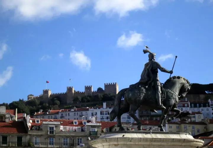 Estatua ecuestre de un rey con el Castillo de San Jorge al fondo, un lugar que ver en Lisboa.