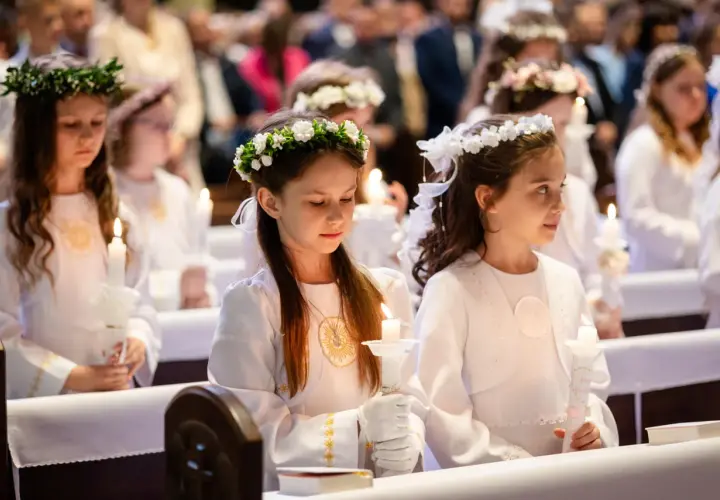 Dziewczynki w białych strojach z wiankami na głowach trzymają świece. Zastanawiasz się, ile kosztuje fotograf na komunie?