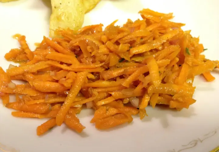 En fransk morotssallad med finstrimlad morot, lök och en lätt dressing. Serveras på en vit tallrik.