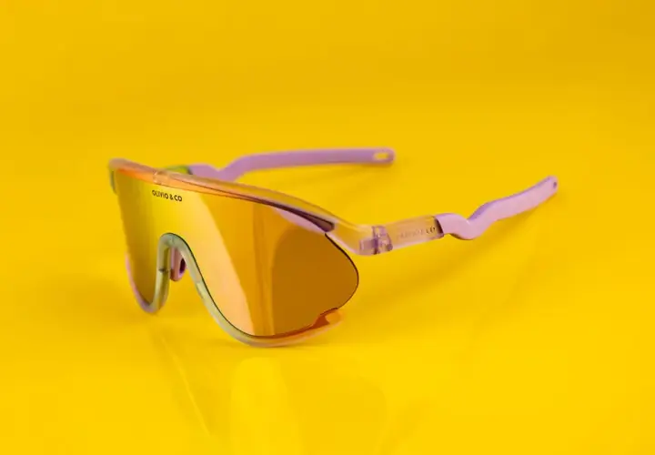 Oto odpowiedź na pytanie: jakie okulary na rower? Stylowe, pomarańczowe okulary sportowe z fioletowymi zausznikami, idealne na rowerową przejażdżkę.