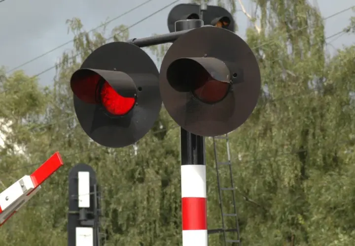 Czerwone światła na przejeździe kolejowo-drogowym ostrzegają przed nadjeżdżającym pociągiem. Zapora jest opuszczona.
