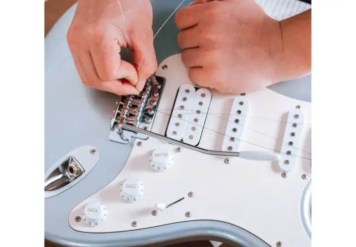 Ręce montują nową strunę w gitarze elektrycznej. Dowiedz się, co ile wymieniać struny w gitarze elektrycznej, by cieszyć się czystym brzmieniem.