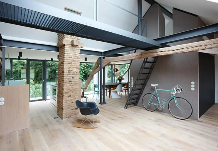 Moderner offener Dachstuhl mit sichtbaren Stahlträgern, Ziegelpfeiler, Holz und einer Leiter. Ein Fahrrad steht bereit.
