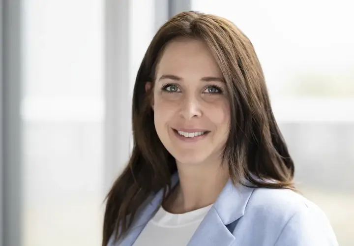 Porträt einer lächelnden Frau mit braunen Haaren und einem hellblauen Blazer. Dies ist eine klare Definition eines Porträts.