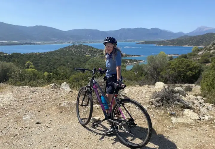 Woman on a bicycle enjoying scenic bicycle tours over 50, with a beautiful blue bay and mountains in the background.