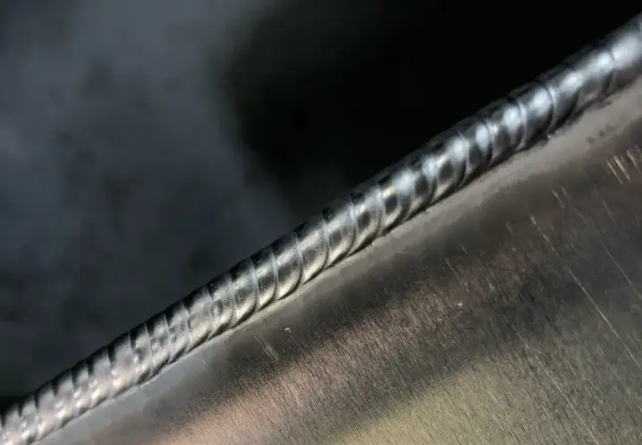 Zbliżenie na idealnie wykonaną spoinę spawalniczą na metalowej powierzchni.