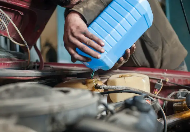 Mecánico vierte líquido refrigerante azul para limpiar radiador coche.