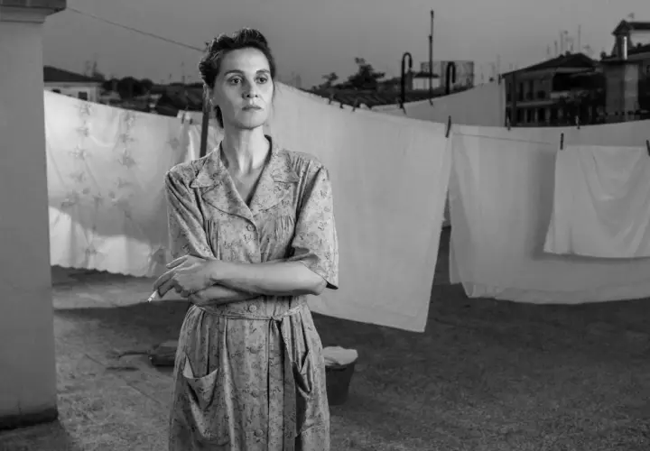 Una donna con un vestito a fiori fuma sul tetto, con panni stesi sullo sfondo. Le recensioni di "C'è ancora domani" lodano la sua interpretazione.
